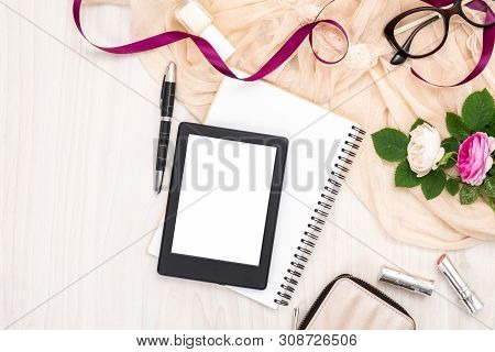 Flat Lay E-book Reader, Glasses, Roses Flowers, Ribbon, Scarf, Paper Note On Wooden Desk. Top View W