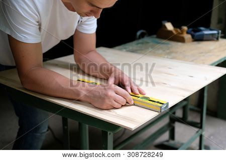 Carpenter Marking Straight Line On Plywood Sheet Using Spirit Level In Carpentry Workshop. Measuring