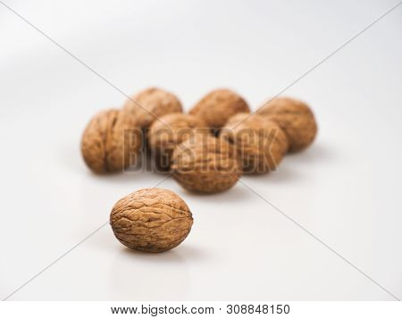 One Walnut (júglans Régia) Close-up In Focus On A White Background, Behind There Are Still Many Nuts