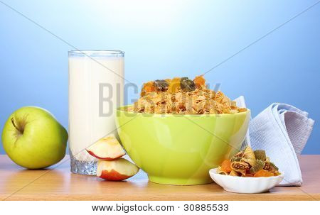 leckere Cornflakes in grüne Schale, Äpfel und Glas Milch auf Holztisch auf blauem Hintergrund