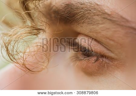 Male Eye Close Up. A Curl Of Curly Hair Hangs Over A Man's Face. Thoughtful Look Into The Void