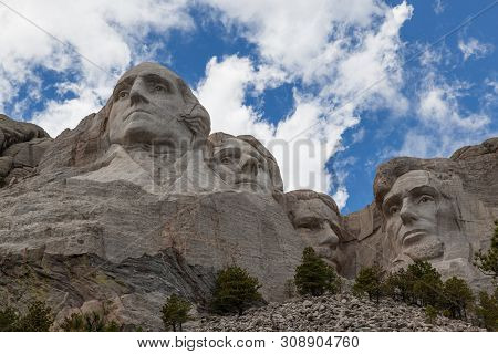 Blue Sky And White Fluffy Clouds Provide A Striking Back Drop For The Carved Faces Of Four Famous Un