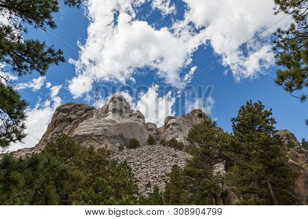 Blue Sky And White Fluffy Clouds Provide A Striking Back Drop For The Carved Faces Of Four Famous Un