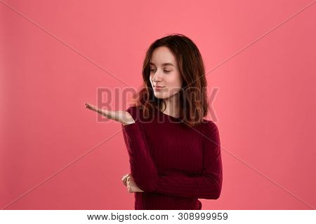Excited Young Lady Standing Isolated Over Dark Pink Background Looking At Empty Space On A Palm Of A
