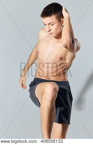Sport Man In Shorts Doing Exercise Leaning Forward On Gray Background