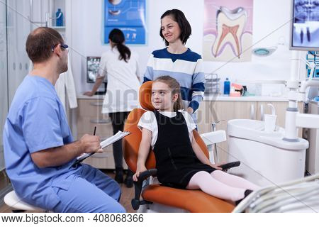 Stomatolog Assistant Discussing About Tooth Hygine Of Kid With Parent In Dental Office. Child With H