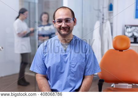 Close Up Portrait Of Orthodontist In Dental Office With Patients In The Background. Stomatolog In Pr