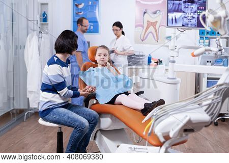 Little Girl Touching Face After Teeth Hygine Treatment With Painful Examining. Child With Her Mother