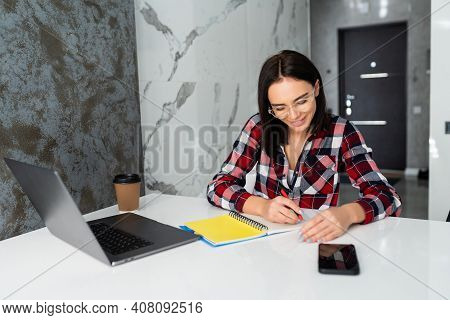 Woman Working On Laptop At Home On Kitchen. Writing On Notepad. Business Woman Thinking About Someth