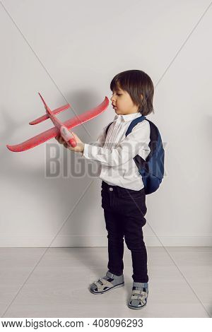 Boy Child In A White Shirt And Jeans Flies On A Red Airplane Toy At The White Wall Of The House