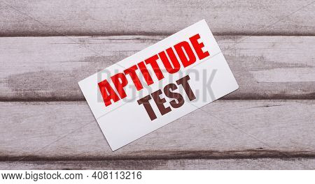 On A Wooden Background, There Is A White Card With Red Text Aptitude Test