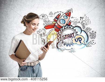 Smiling Young Woman In Casual Clothes With Phone And Notebooks, Standing Over Concrete Wall With Col