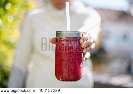 The Girl Holds A Berry Smoothie In A Glass Jar. Proper Nutrition. Orange, Red Berries And Banana Smo