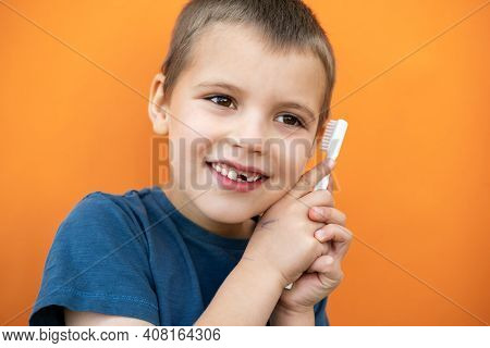 Boy Without Milk Upper Tooth In Blue T-shirt Holds Toothbrush In Hand On The Orange Background.