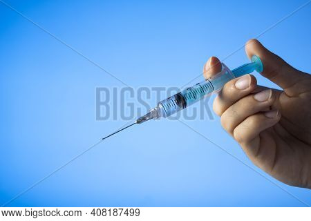 Hand Holding An Syringe With Vaccine. Covid-19 Coronavirus. On Bluebackground