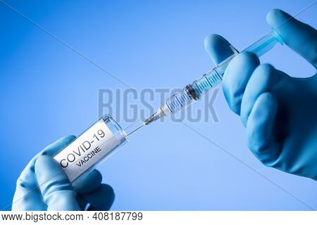 Doctor Filling Syringe With Coronavirus Covid-19 Vaccine. On Blue Background