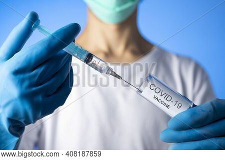 Doctor Filling Syringe With Coronavirus Covid-19 Vaccine. On Blue Background