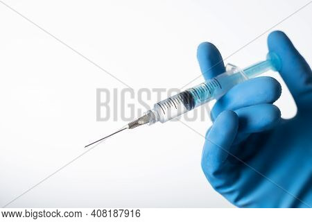 Hand With Blue Gloves Holding An Syringe With Vaccine. Covid-19 Coronavirus. On White Background