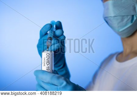 Doctor Filling Syringe With Coronavirus Covid-19 Vaccine. On Blue Background