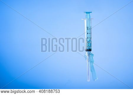 Syringe With Protection Cap On Blue Background. Vaccine Preventions. Copy Space.
