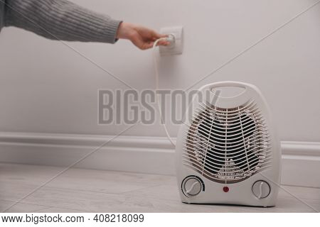 Woman Plug In Modern Electric Fan Heater Indoors, Focus On Device. Space For Text