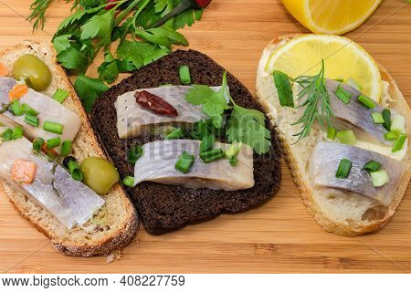 Different Open Sandwiches Made With Slices Of Pickled Herring Fillet And Various Bread Kinds On A Wo