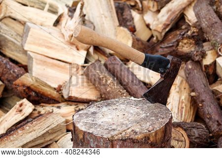 An Axe On A Wood, Tree Log. An Axe Stuck In A Log In Front Of A Pile Of Wood, Ready For Chopping And