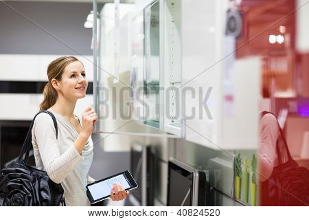 Ung kvinde shopping for møbler i en møbelforretning, ved hjælp af hendes tablet computer for at sammenligne priser