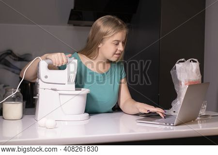 A Blonde Woman Videoblogger Cooking In Modern Kitchen Near Laptop, Online Learning Or Remote Cooking