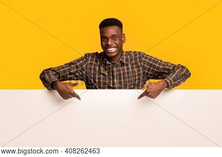 Free Place For Ad. Cheeful Black Guy Pointing Down At Blank White Advertisement Board, Happy Africam