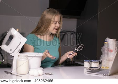 A Blonde Woman Videoblogger Cooking In Modern Kitchen Near Laptop, Online Learning Or Remote Cooking