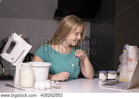 A Blonde Woman Videoblogger Cooking In Modern Kitchen Near Laptop, Online Learning Or Remote Cooking