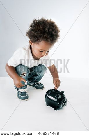 Portrait of a Nice African American Child Putting Coins in to the Pig-shaped Money Box. Isolated on Grey White Background. Hope for Better Future