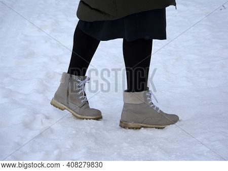 A Woman Walks Along A Snow-covered Forest Path In A Nature Park On A Walking Path, She Is Wearing Wh