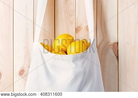 White Eco Bag Full Of Lemons Hang On Wood Wall Close-up. Whole Citrus Fruit For Detox In Larder