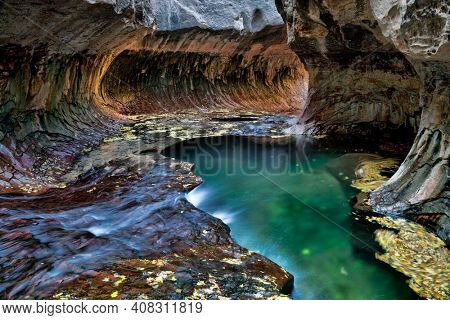 Green pool, swirling leaves and flowing water with a circular rock formation at the Subway, a unique tunnel scuplted by the Left Fork of North Creek in Zion National Park, Utah