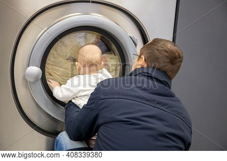 Prague, Czech Republic - 16.12.2020: Man With His Baby Waiting For Laundry In Laundry Room With Spee