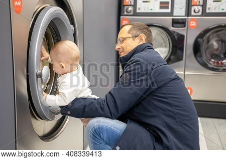 Prague, Czech Republic - 16.12.2020: Man With His Baby Waiting For Laundry In Laundry Room With Spee