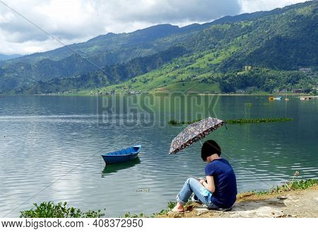 Young Woman Sitting Peacefully Beside Phewa Lake, With Beautiful Mountainous Scenery In Background, 