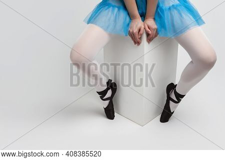 Legs Of Caucasian Female Ballet Dancer In Pointes Shoes And Blue Skirt Sitting On High Cube Against