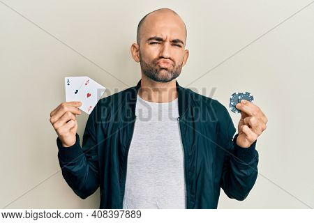 Young hispanic man playing poker holding casino cards and chips looking at the camera blowing a kiss being lovely and sexy. love expression. 
