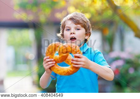 Adorable Little Kid Boy Eating Huge Big Bavarian German Pretzel. Happy Blond Child Enjoying Tasteful
