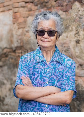 Senior Woman With Short Gray Hair Wearing Glasses, Arms Crossed, Smiling, And Looking At The Camera 