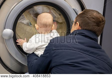 Prague, Czech Republic - 16.12.2020: Man With His Baby Waiting For Laundry In Laundry Room With Spee