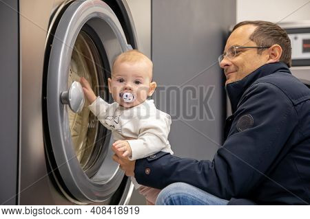 Prague, Czech Republic - 16.12.2020: Man With His Baby Waiting For Laundry In Laundry Room With Spee