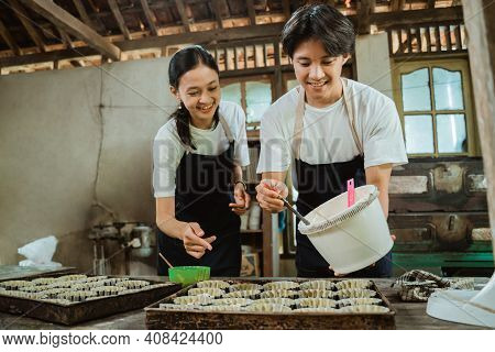 Smiling Asian Couple Wearing An Apron While Pouring Dough On A Cake Pan