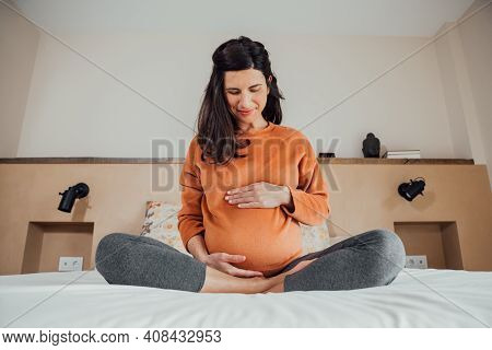 Front View Of Beautiful Long Hair Brunet Caucasian Pregnant Woman, Sitting In Crossed Legs In Bed, I