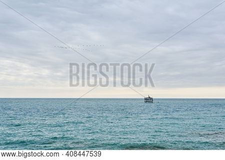 Seascape With Mariculture Installation In The Distance And Flock Of Birds In Cloudy Sky