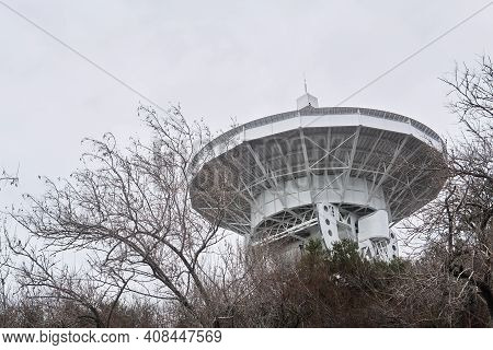 Mirror Of A Large Astronomical Radio Telescope, Aimed At A Cloudy Sky, Is Visible From The Trees