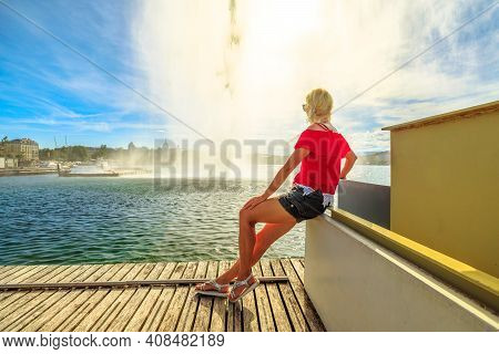 Tourist Girl Sitting On E Wooden Jetty, Looking Jet Deau Fountain Which Projects Its Water Spray 140